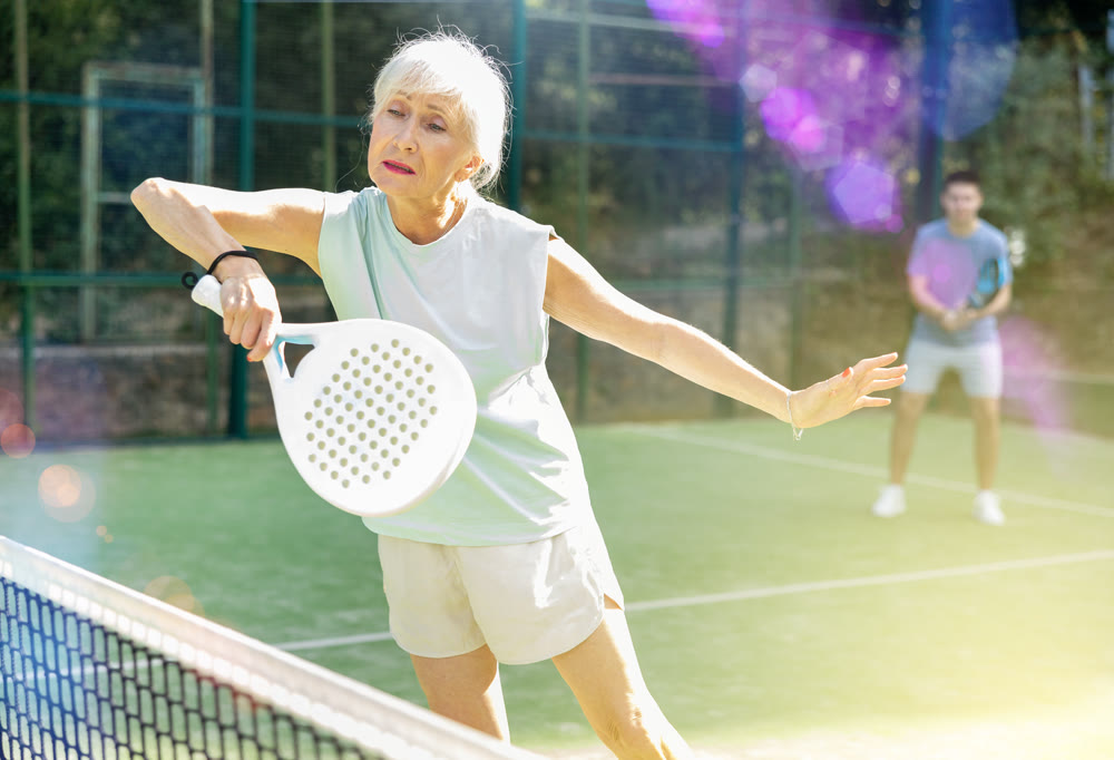 Concentrated elderly woman padel player hitting ball with a racket on hard court