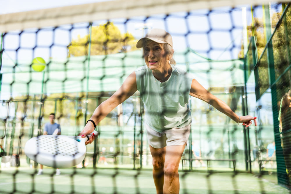 View through tennis net of an mature female playing padel