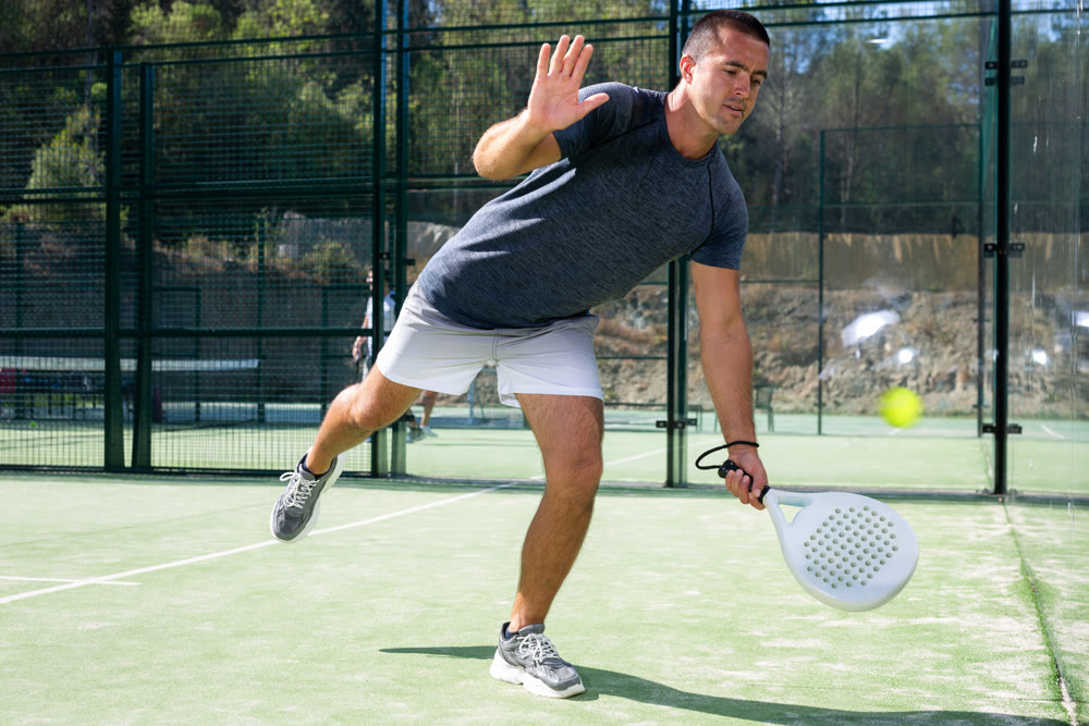 Paddle tennis player preparing to perform left-handed forehand on outdoor court