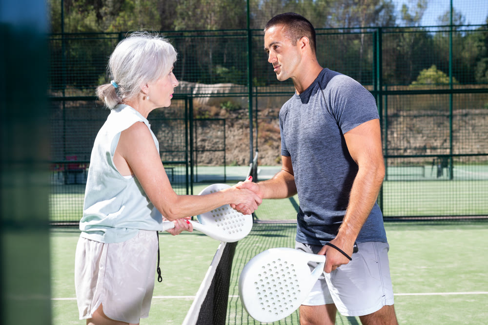 Young man and senior woman handshaking after padel tennis match
