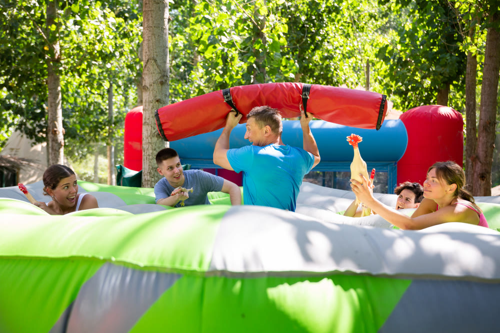 Playful man fighting off friends with inflatable log while guarding toy chickens