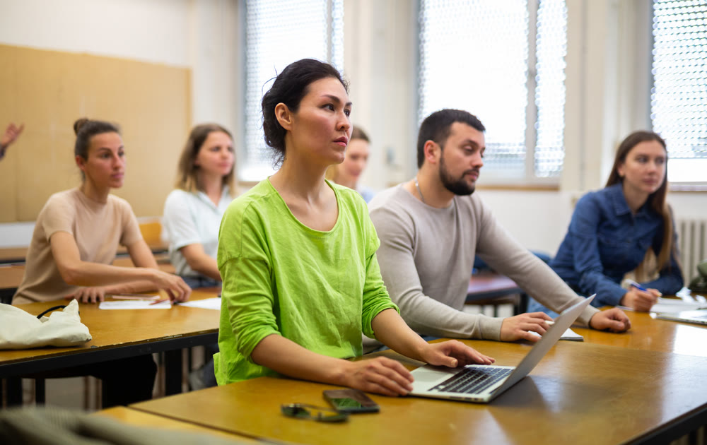Female student writing lectures in workbooks and laptop in classroom during lesson