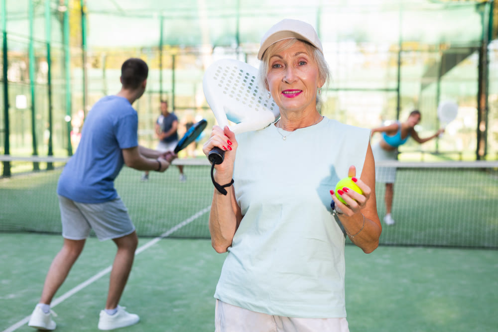 Mature woman posing with racket and ball in hands on padel court