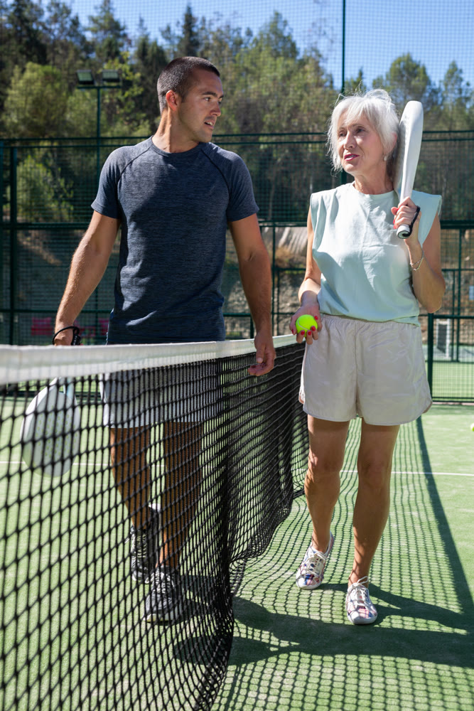 Man and elderly woman walking along tennis net on open court after match