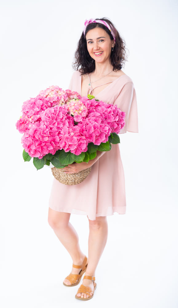 Portrait of happy adult woman with basket of pink flowers on white background