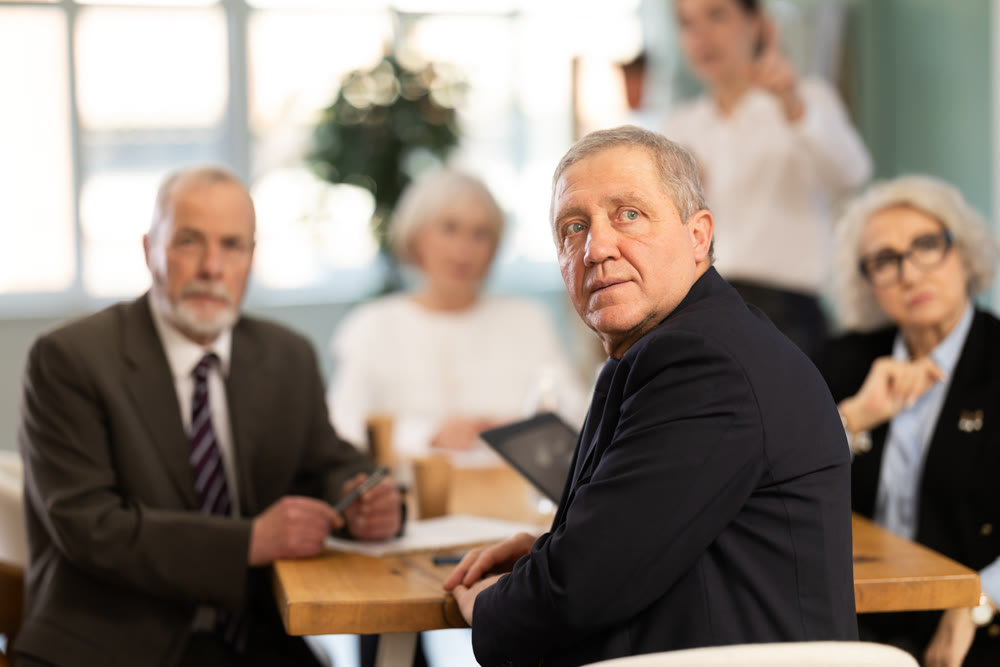 Office coworkers watching presentation while sitting at table with laptop, notes