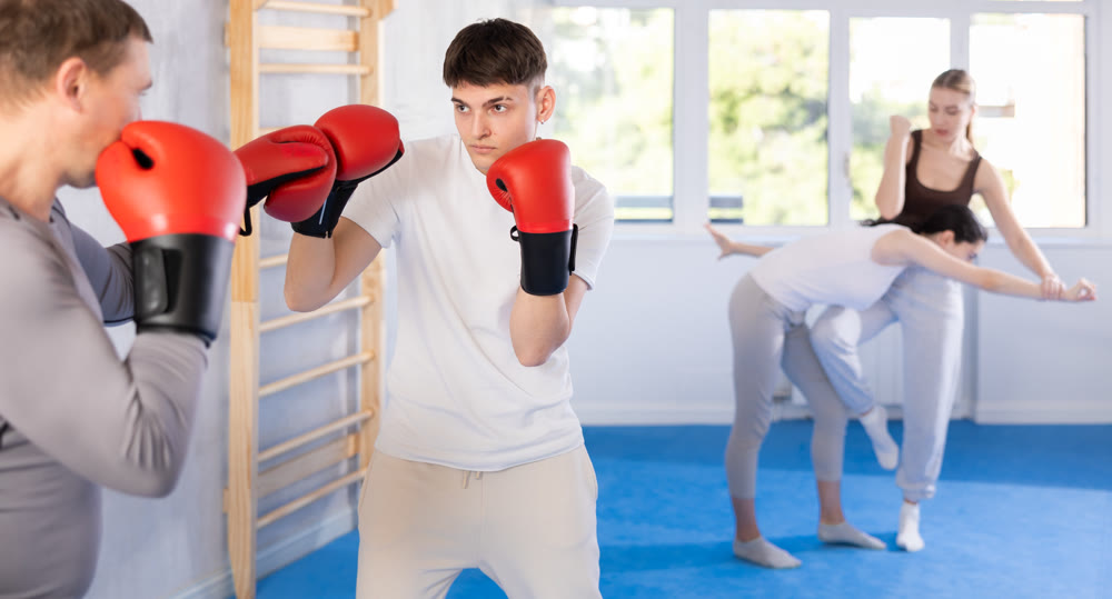 Young guy training boxing kicks on punch mitts held by instructor