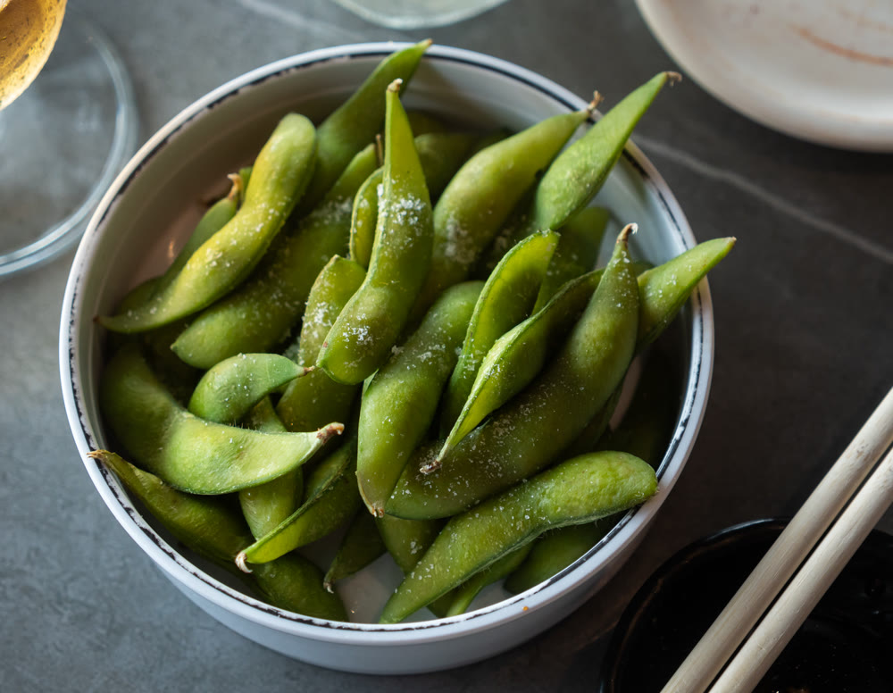 Steamed edamame sprinkled with sea salt on dark stone board, top view