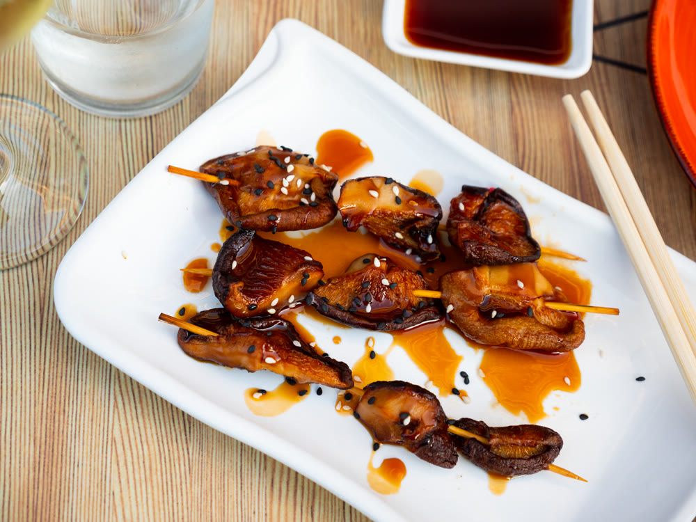 Close-up of grilled mushroom skewers seasoned with balsamic vinegar and sesame seeds
