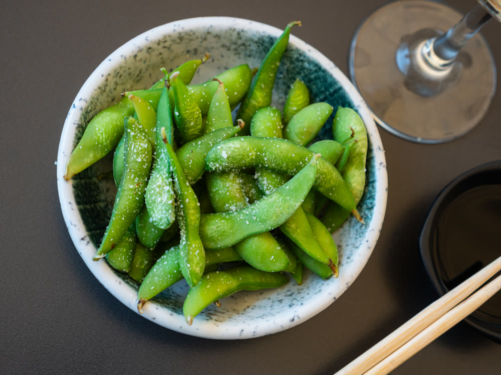 Steamed edamame sprinkled with sea salt on dark stone board, top view