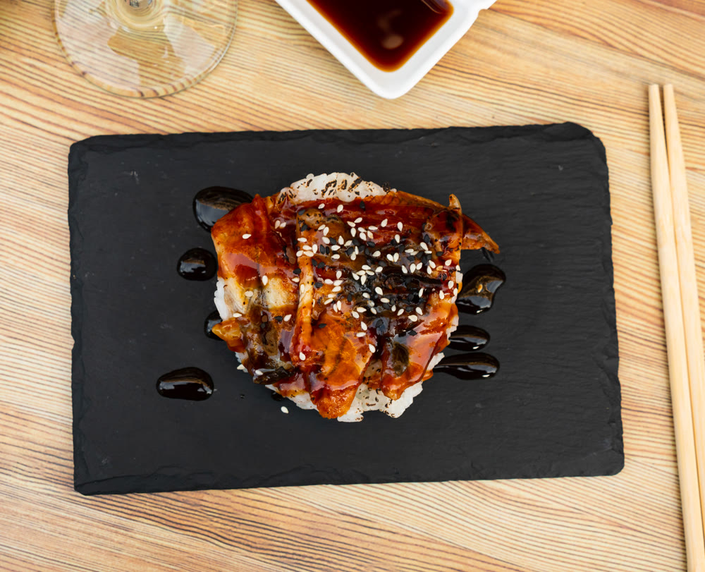 Japanese appetizer with fried eel, saucer and rice on a stone stand with chopsticks