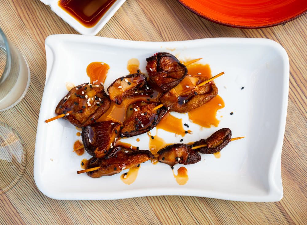 Close-up of grilled mushroom skewers seasoned with balsamic vinegar and sesame seeds