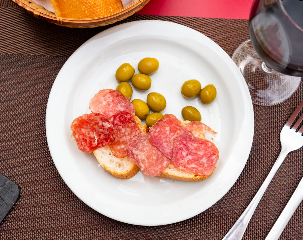 Smoked sausage sandwich and green olives on plate - an appetizing snack