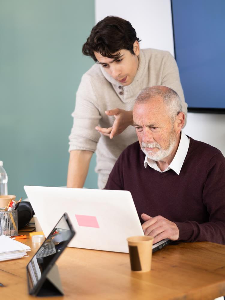 Guy helps elderly man complete task on laptop