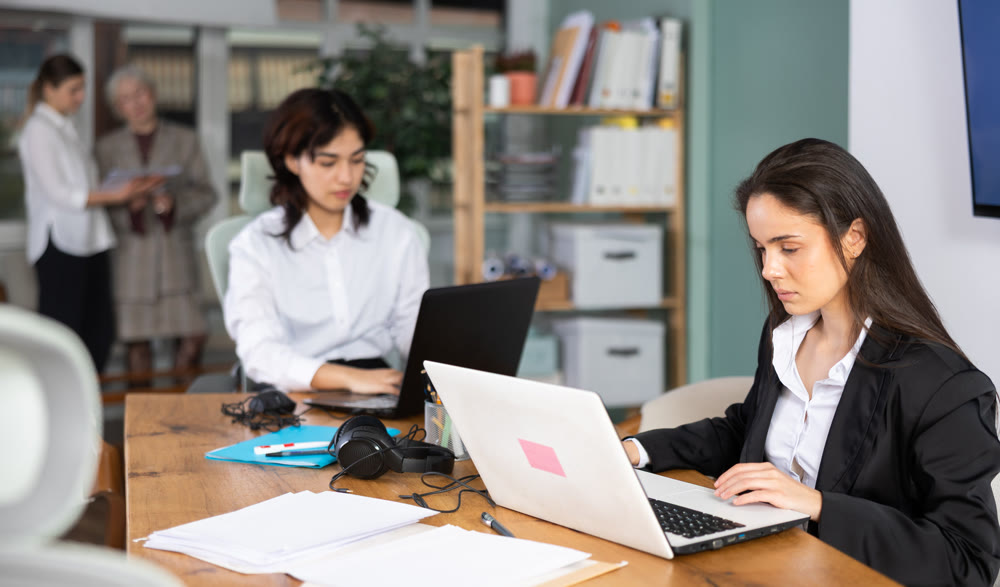 Young woman works on laptop with female colleagues