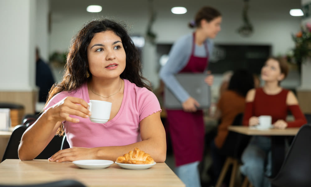 Young Latina girl enjoying coffee and croissant in cafeteria