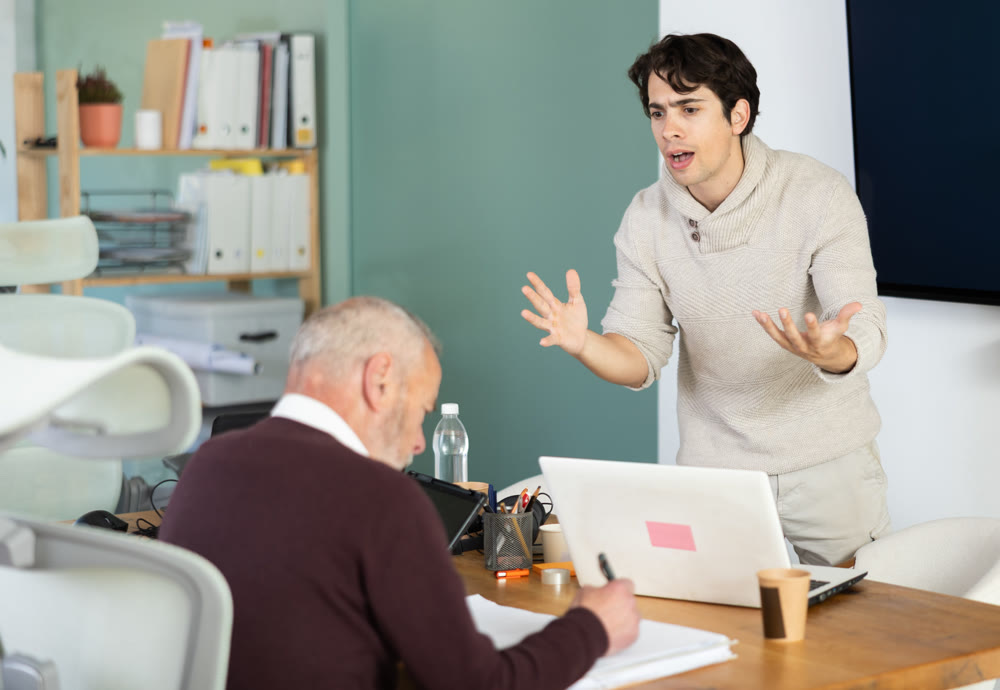 Young man scolding elderly man working with documents in office