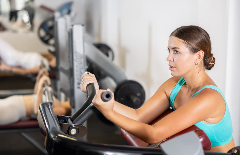 Sporty girl pumps up her arm muscles on a special exercise machine in gym