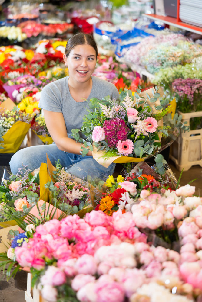 Young woman customer choosing bouquet of flowers in open-air plants market