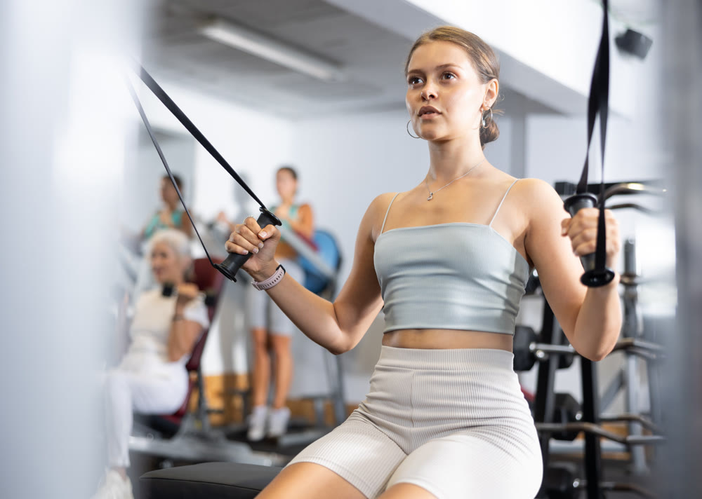 Athletic woman working on special machine with ropes to develop arm muscles