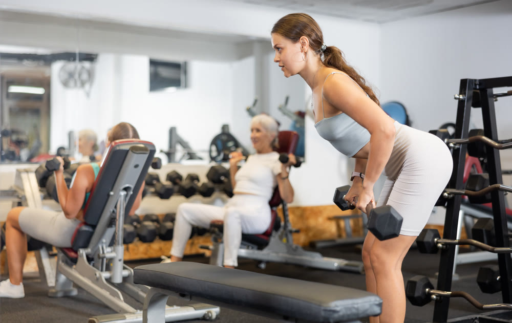 Slender girl trains muscles of arms and back using barbell and differentiated weighting in gym