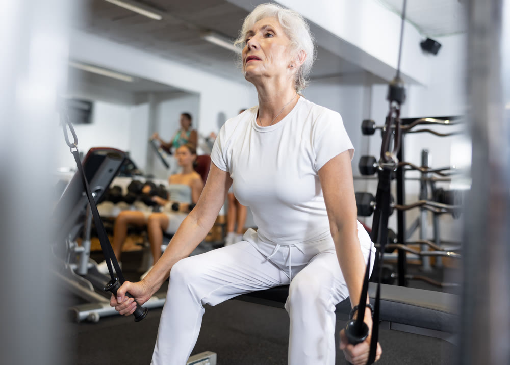 Mature woman working on special machine with ropes to develop arm muscles
