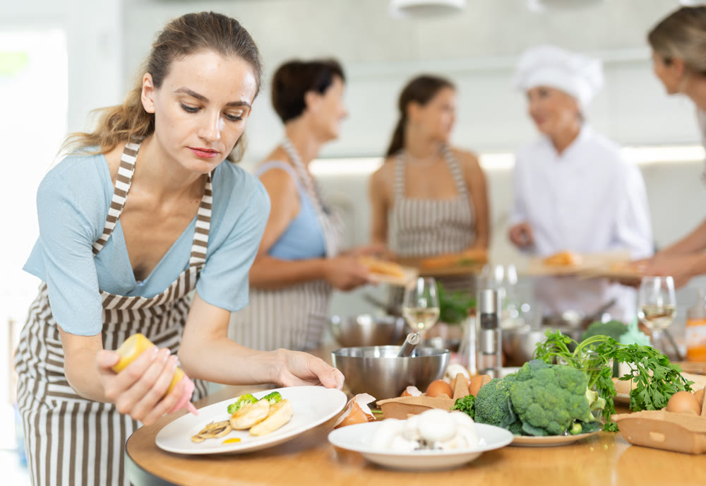 Girl visitors to culinary school decorates finished dish, fried chicken fillet with golden crust.