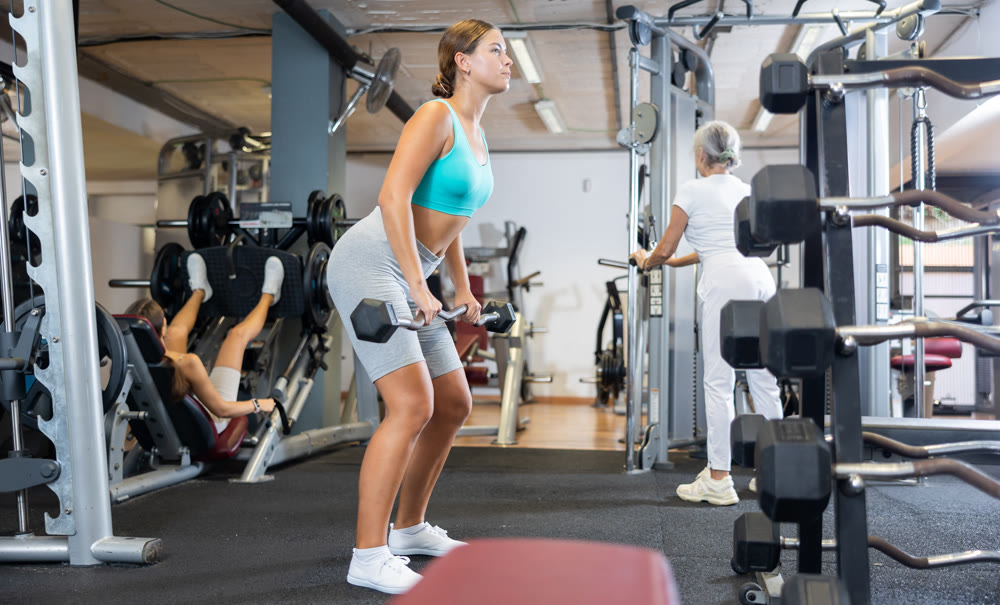 Focused sporty girl performing set of exercises with barbell during intense workout. Concept of weight training