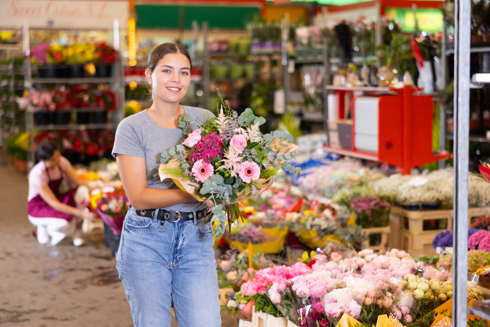Cheerful girl choosing floral arrangement amidst flower market stalls