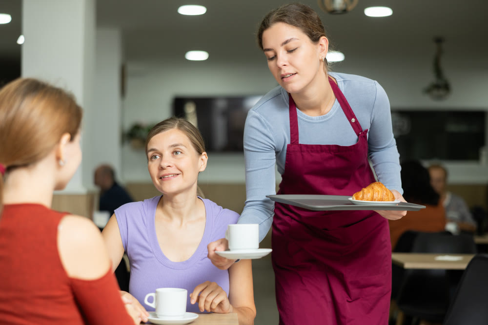 Friendly waitress brought croissants and coffee to female customers