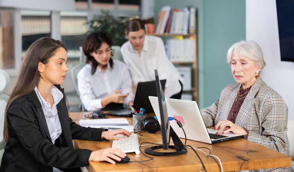 Young woman works on laptop with female colleagues