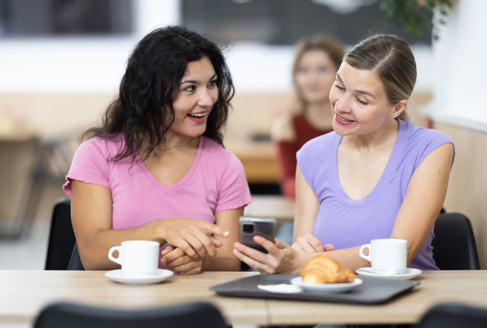 Happy smiling attractive girl emotionally discussing with female friend while dining in restaurant