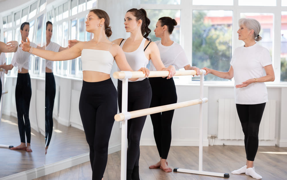Teacher conducts class with girls in ballet studio, observes doing third position exercise.