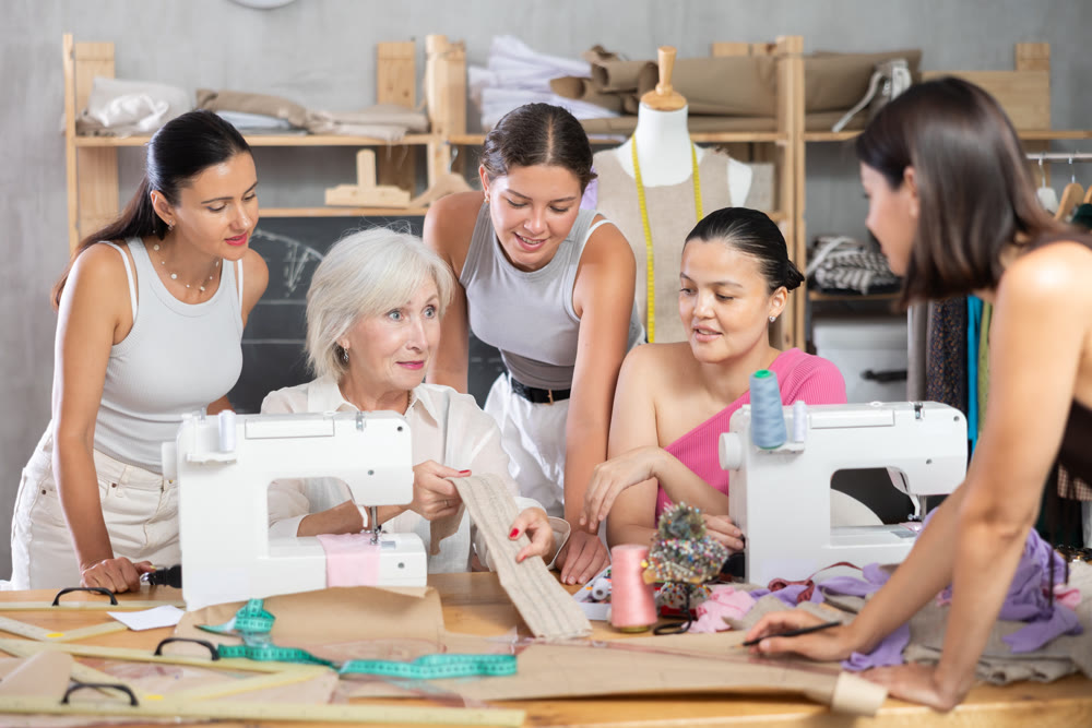 Elderly female teacher shows group how to sew