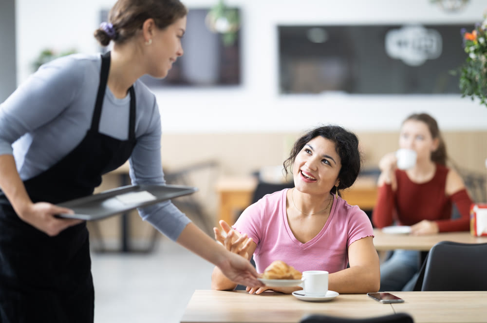 Friendly waitress brought croissants and coffee to female customer