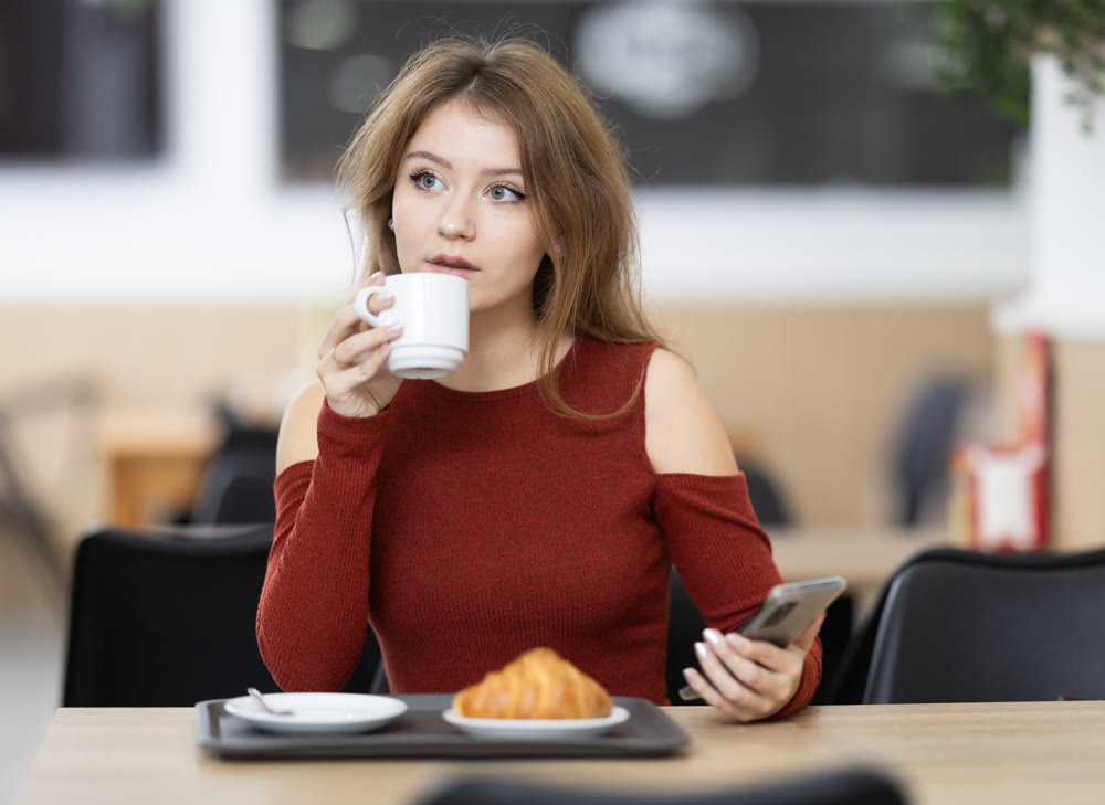 Young female sitting alone at table in cozy cafe, drinking fragrant coffee