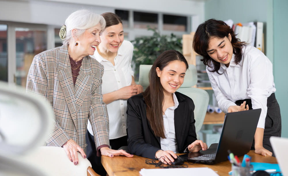 Group of women colleagues look at laptop screen and laugh