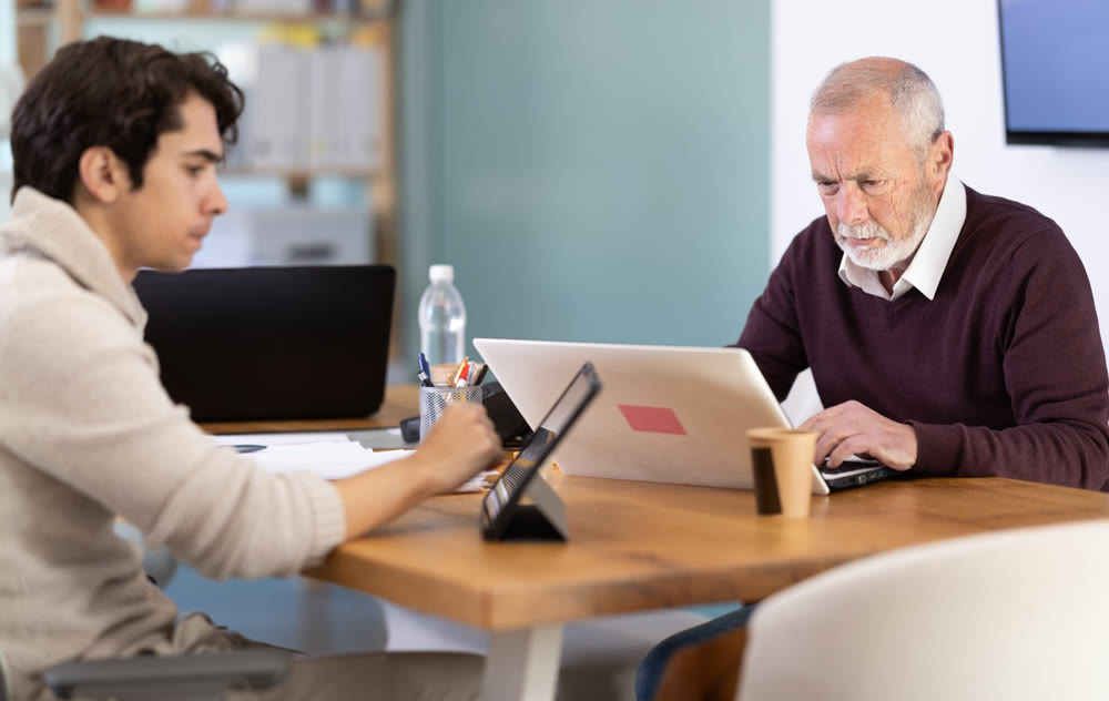 Two male manager work on laptops in modern company office