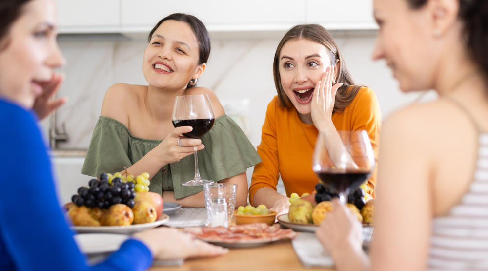 Four women are sitting at table, enjoying food and wine, chatting, talking, laughing.