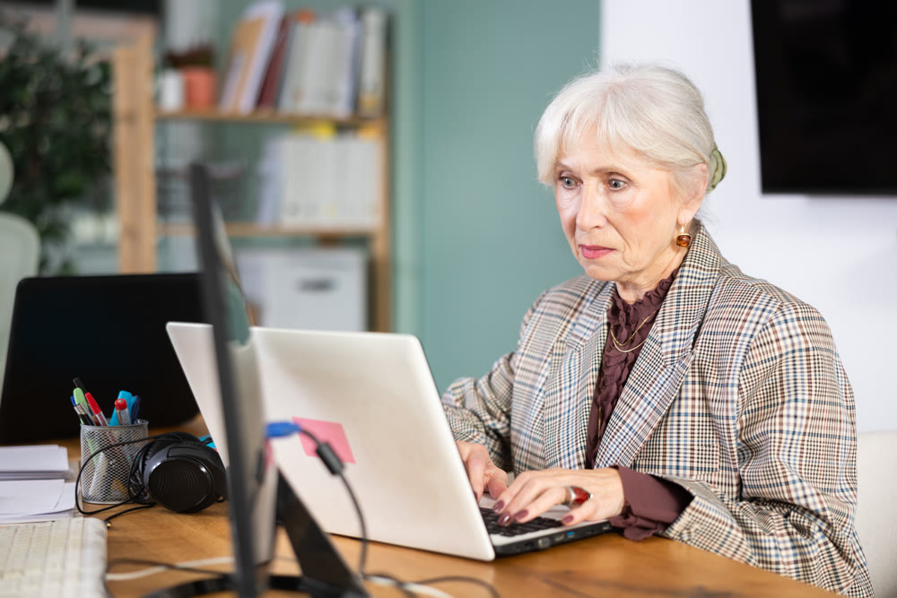 Senior woman sitting at desk is working on laptop computer