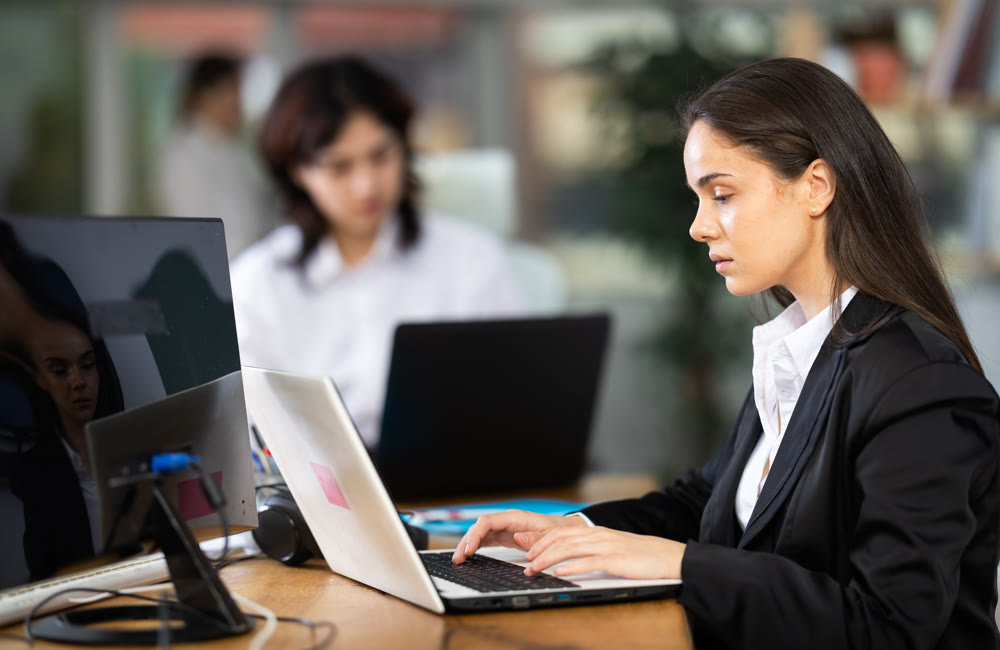 Young woman works on laptop with female colleagues