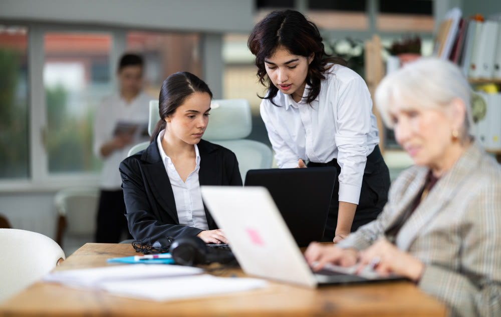 Young woman helping colleague work on laptop in office