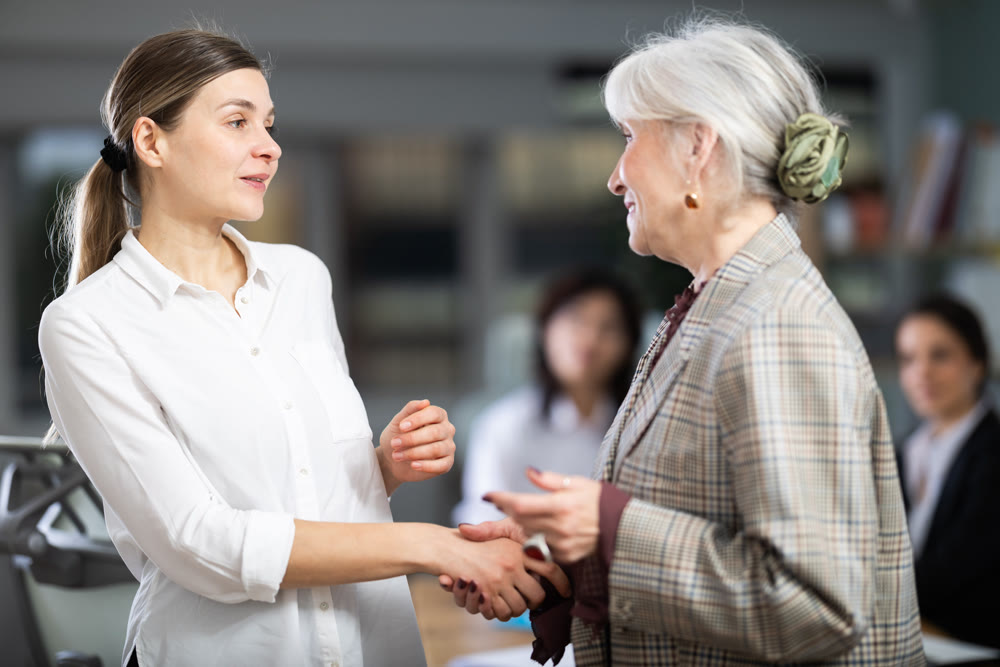 Adult and elderly woman shaking hands in office