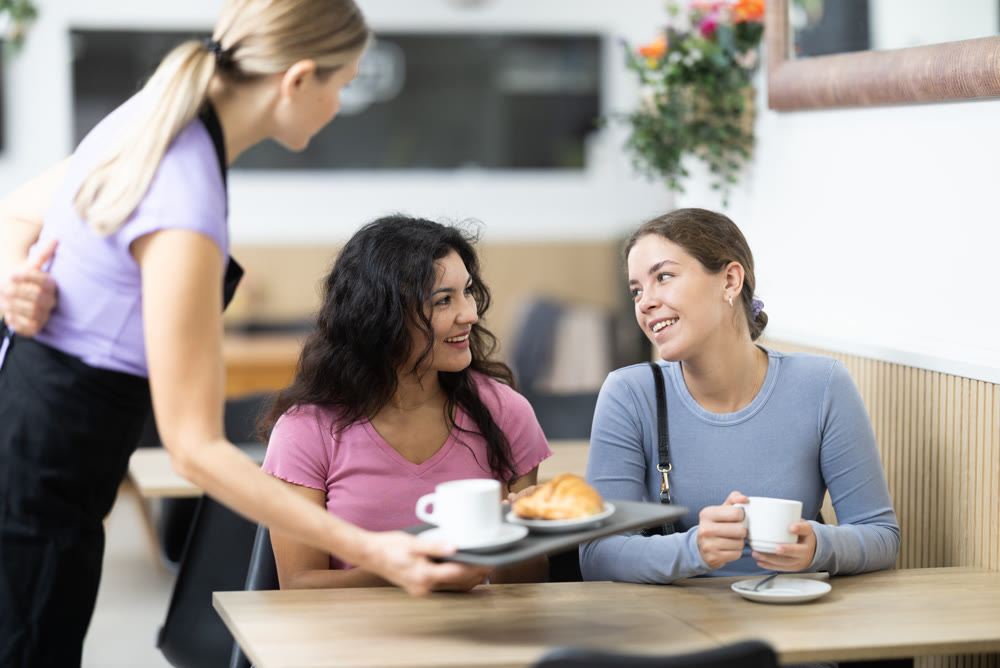 Adult female waitress serves coffee and croissant