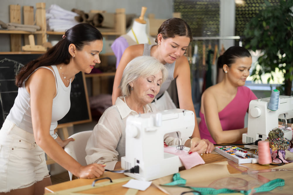 Mature female instructor demonstrating stitching at machine to younger wome