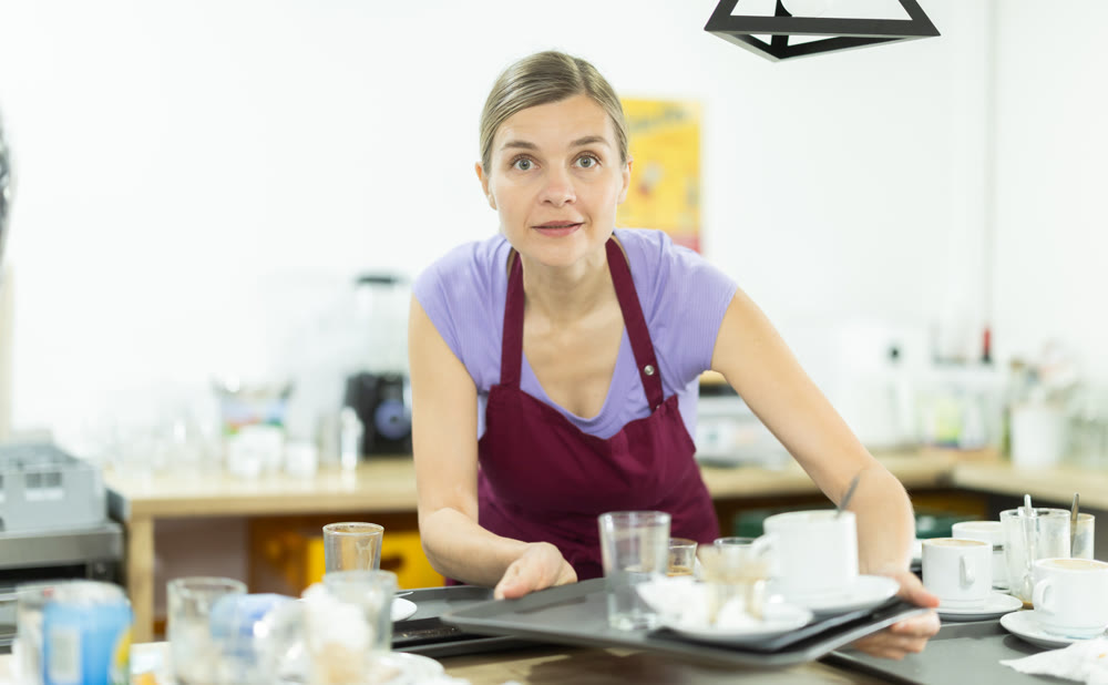 Cafe waitress with a tray of dirty dishes in cafe interior