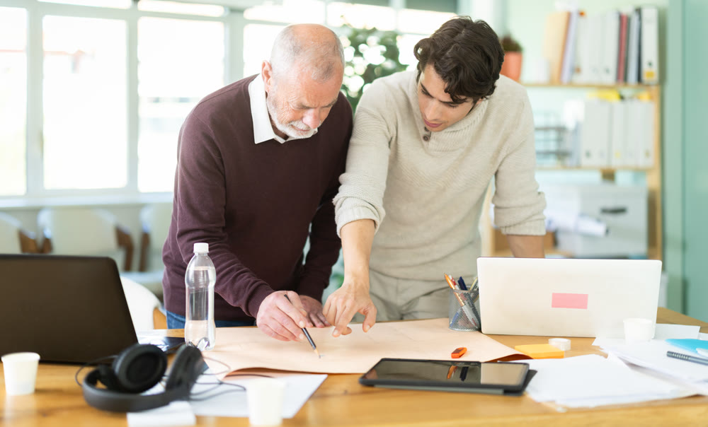 Young and elderly men colleagues discussing building plan in office