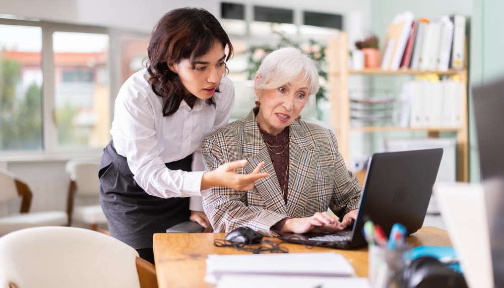 Young girl helping mature colleague with tasks on laptop