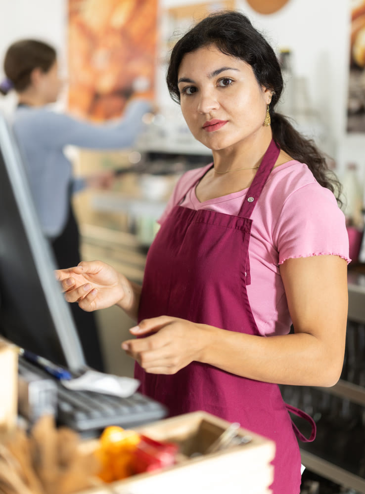 Attentive young waitress checking orders on monitor in cafeteria