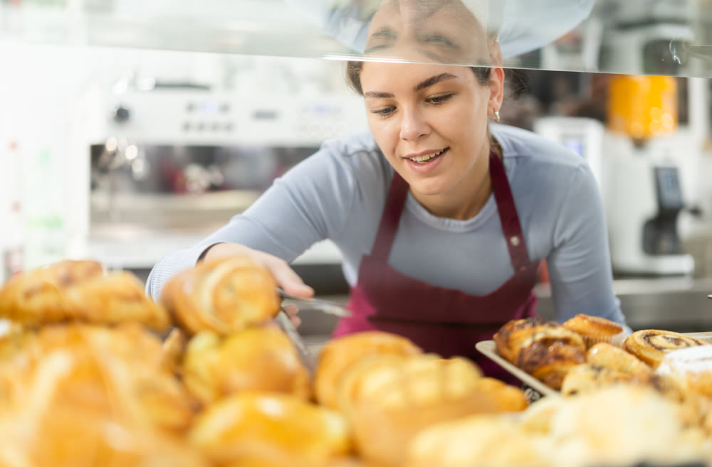 Woman seller putting fresh pastries on plate in cafe bakery